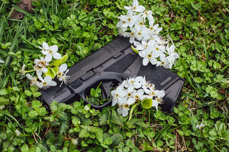 A Springfield Armory Hellcat pistol in a green field of clover with white briar flowers