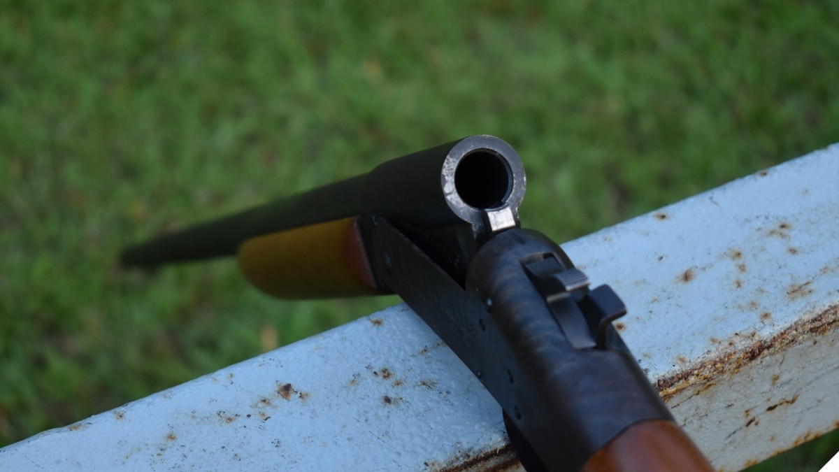 A break action single shot shotgun over a fence rail, unloaded