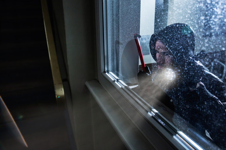 Burglar With Crowbar And Flashlight Looking Into A House Windows